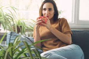 Content woman drinks coffee on her couch after finding relief from PTDS symptoms with EMDR therapy in Burke, VA at Nova Terra Therapy 22015