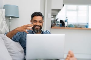 latino man sitting at the computer looking happy during online therapy in Virginia with an online therapist from Nova Terra Therapy